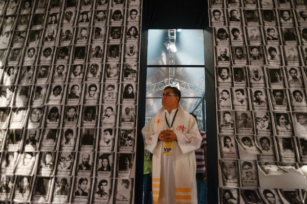 A priest stands in the "Hall of the Lost and the Disappeared," where photographs of victims of forced disappearances are plastered on the walls. (Photo by Eloisa Lopez)