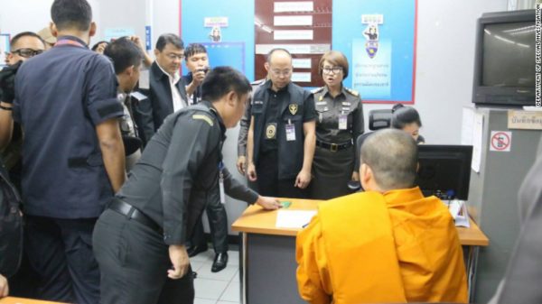 Wiraphon, wearing the orange robes of the monkhood, is processed by Thai immigration authorities.