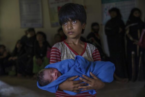 Rohingya Muslim girl Afeefa Bebi, who recently crossed over from Myanmar into Bangladesh, holds her few-hours-old brother as doctors check her mother Yasmeen Ara at a community hospital in Kutupalong refugee camp, Bangladesh, Wednesday, Sept. 13, 2017. The family crossed into Bangladesh on Sept. 3. (AP Photo/Dar Yasin)